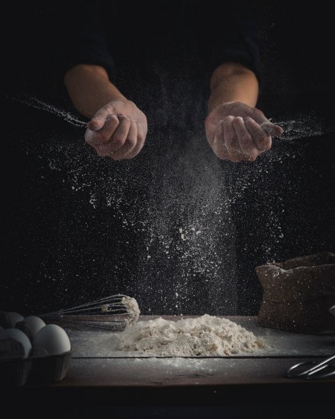 person sprinkling flour on kitchen board