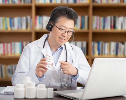 asian doctor sitting in front of laptop holding pill bottle