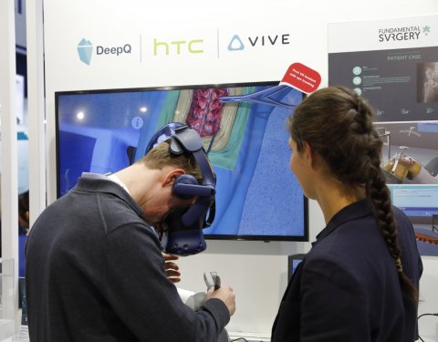 man wearing vr headset in front of surgery scene on a display. on the right side, a woman is standing, with the back of her head visible