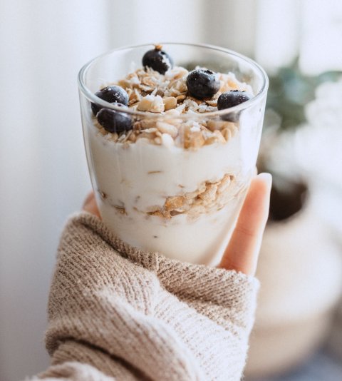 female hand holding a glass of yoghurt with cereals and berries