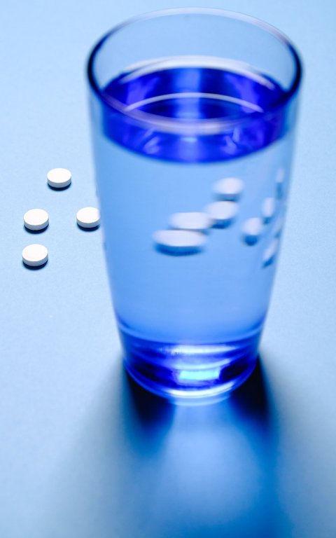 drinking glass filled with water and white pills on blue background