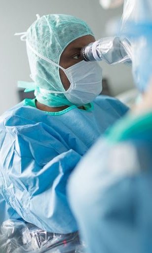 man in surgical gown using a microscope