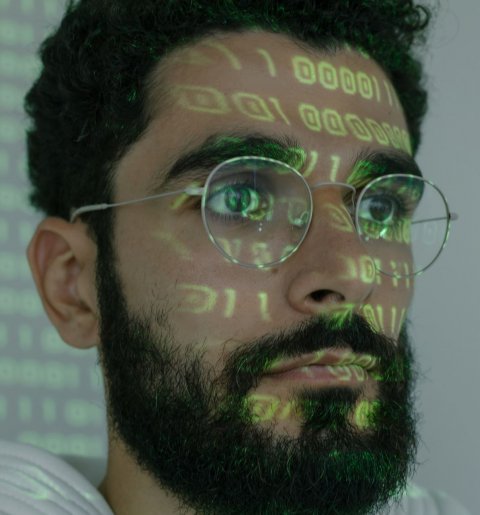 man with glasses and beard with digital binary code projected on his face