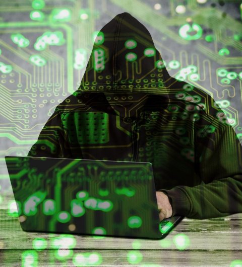 man in hooded sweater sitting in front of laptop with circuitry background