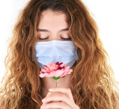 young woman with blue face mask smelling a pink flower