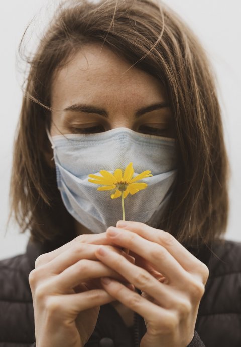 woman wearing face mask smelling a yellow flower