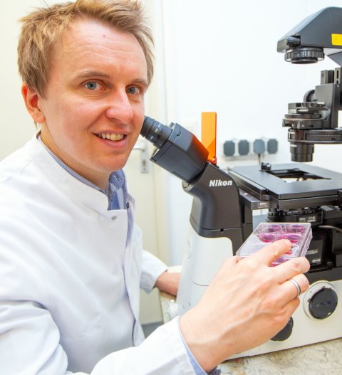 scientist in white lab coat sitting next to microscope