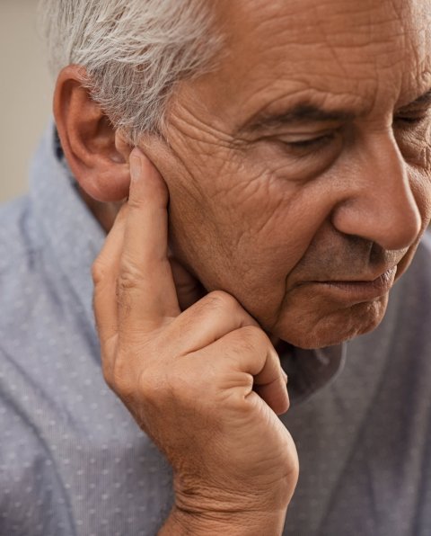 senior man with hearing problems, touching his ear with his hand
