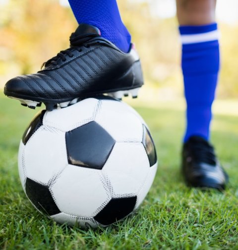 closeup photo of soccer ball under football shoe on grass flied