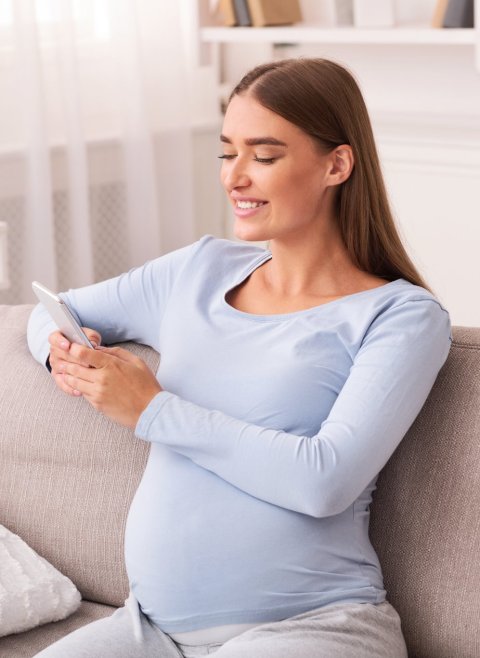 pregnant woman holding a smartphone sitting on white sofa