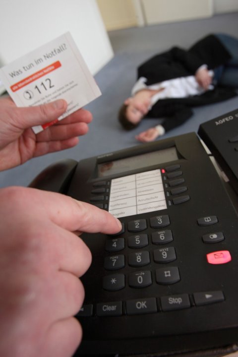 hand dialling german emergency number 112 on telephone, unconscious person in the background