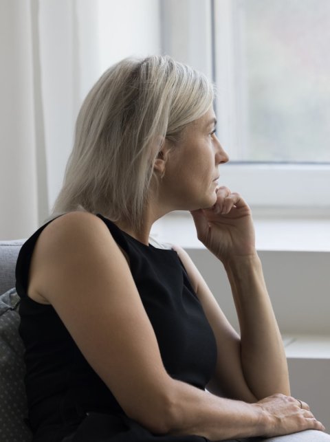 A sad looking older woman sitting on a sofa, looking out of the window