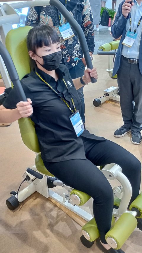 Young woman presenting fitness bench device at a healthcare exposition booth