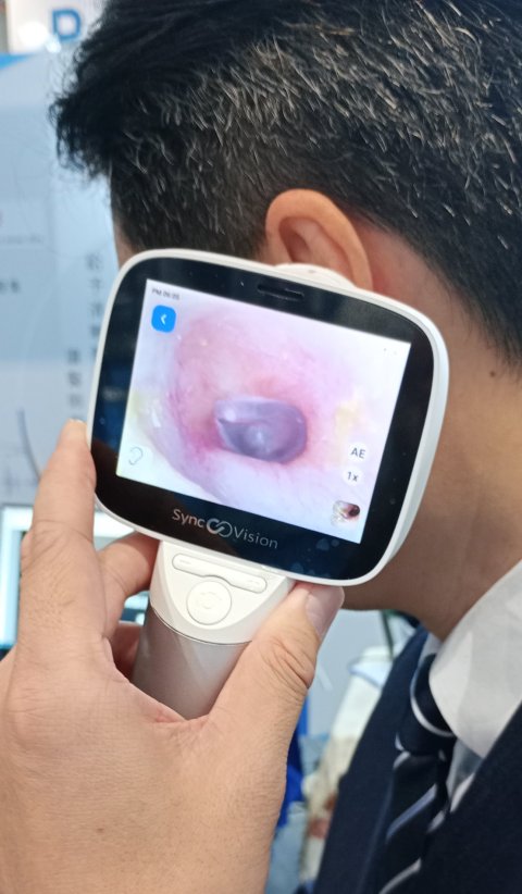 A man holds a handheld ENT scanner to his ear