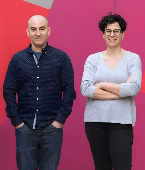 Dr. Núria López-Bigas and Dr. Abel González-Perez standing next to each other in front of a colorful red and pink wall