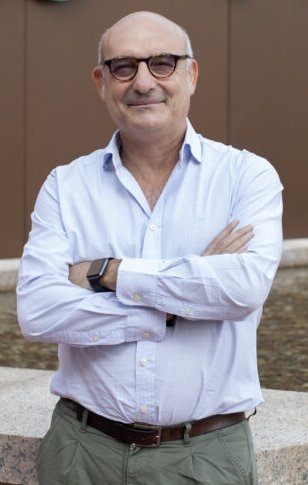 Joaquín Martínez is standing with his arms crossed in front of his chest, in front of a building with the sign cnio stop cancer