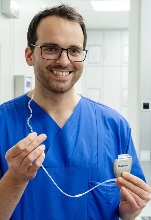 Dr Leonard Bergau hält einen implantierbaren Defibrillator mit Kabel in den Händen