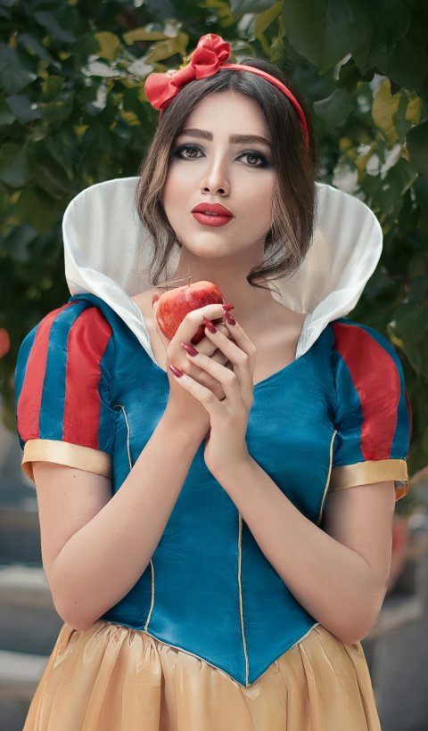 A young woman in cosplay dress as Disney princess Snow White, holding an apple