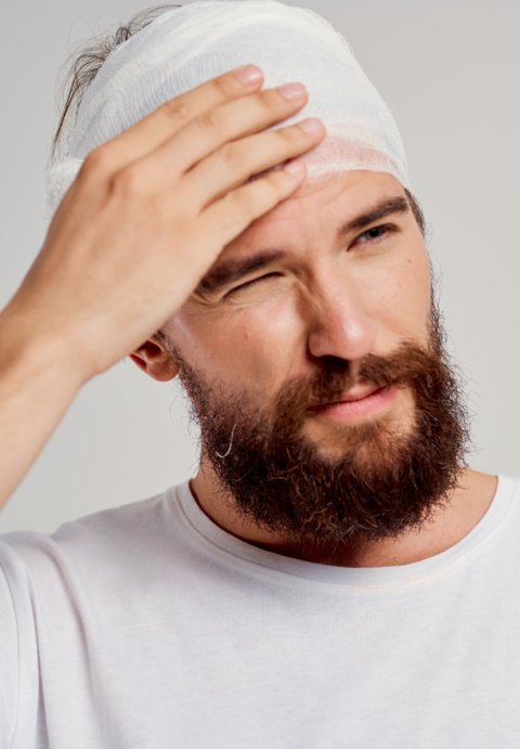 A beaded man with a bandage around his head holding his head from headache pain