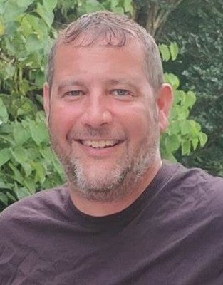 Portrait photo of Lance Thurlow, PhD in front of a background with green leaves