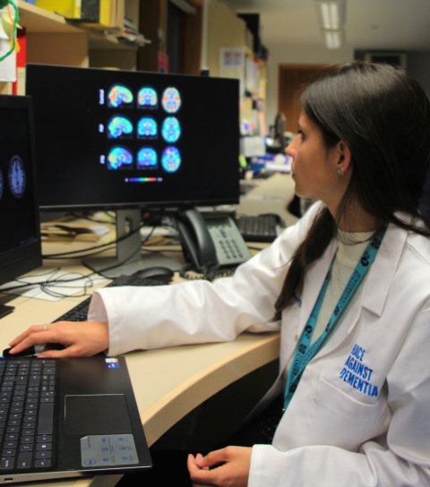 Dr Maura Malpetti is stitting at a desk in front of a laptop computer. She is looking at monitors displaying brain scans