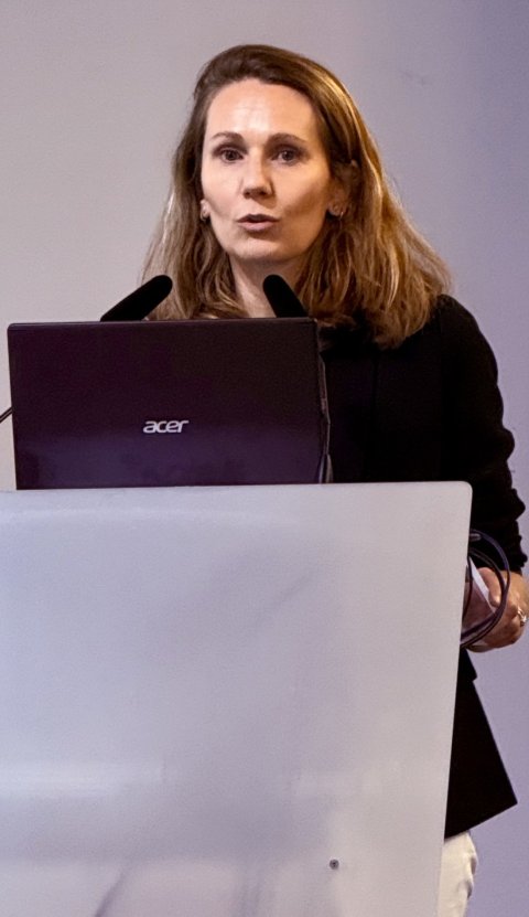Dr Aurélie Dehaene standing behind a speaker's desk, giving a presentation