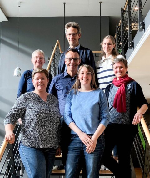 Eine Gruppe von sieben Menschen hat sich auf einer Treppe für ein Gruppenfoto aufgestellt