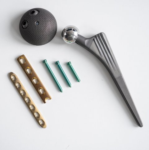 An artificial hip joint implant and assorted metallic screws and scaffolds on a light grey surface