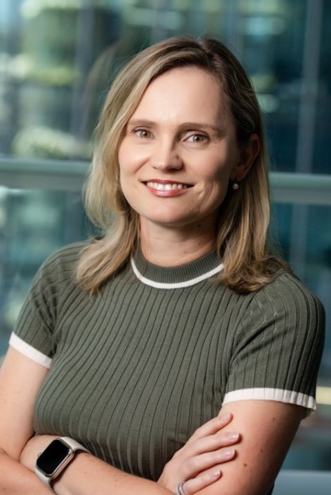 Alta Schutte, Ph.D., is standing with arms crossed in front of her chest, in front of a blurry glass window building front