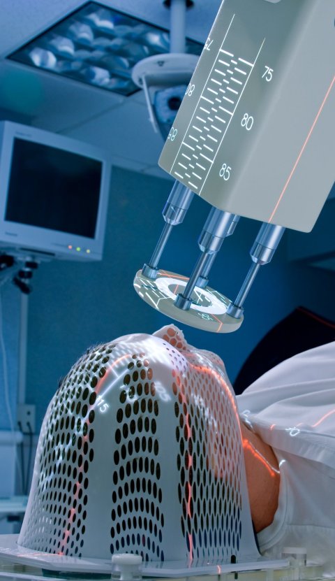 Ein Mann unterzieht sich einer Strahlentherapie. Er trägt eine spezielle Maske über das Gesicht und liegt unter einem Radiotherapie-System