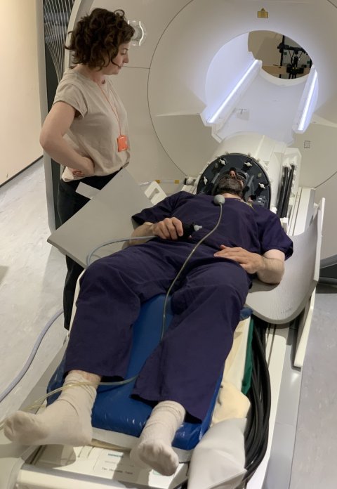 A person wearing a deep brain stimulation helmet is about to undergo an fMRI scan. On the left, a medical imaging professional is supervising the examination