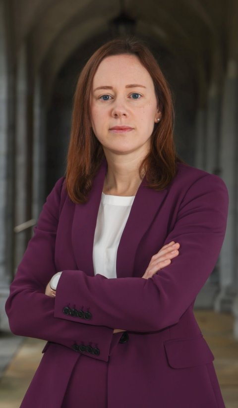 Professor Emer Mggrath standing in an arched hallway with her arms crossed in front of her