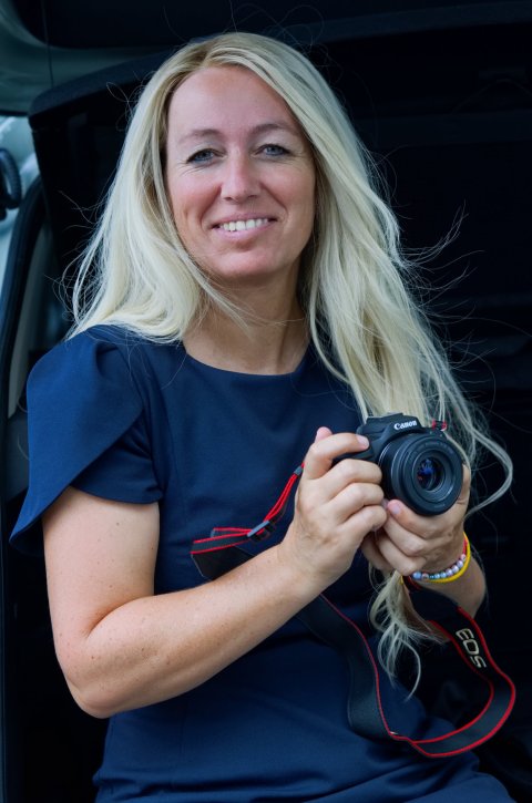 Anja Fink hält eine Spiegelreflexkamera in beiden Händen und lächelt in die Kamera
