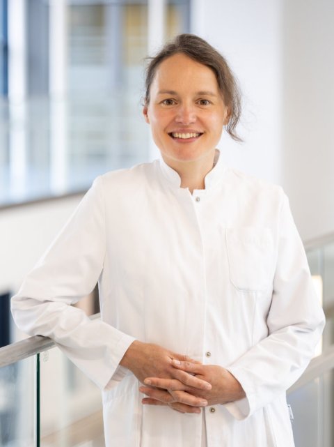Prof. Waltraud Pfeilschifter lehnt im weißen Arztkittel an einem Geländer und lächelt in die Kamera