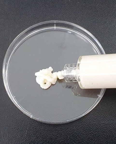 A tube filled with a white paste dispensing a strand of said paste onto a petri dish