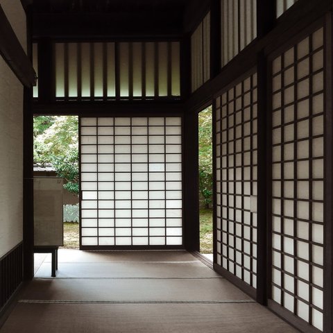 The interior of a traditional Japanese building, like a tea house or historic residence, with translucent paper sliding sdoors with dark wooden grid frames and tatami flooring