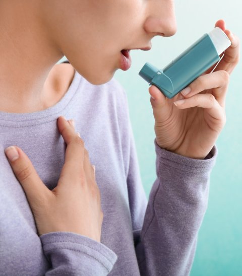 A young woman is using her inhaler against asthma. Her right hand is on her thorax, to emphasize airway obstruction