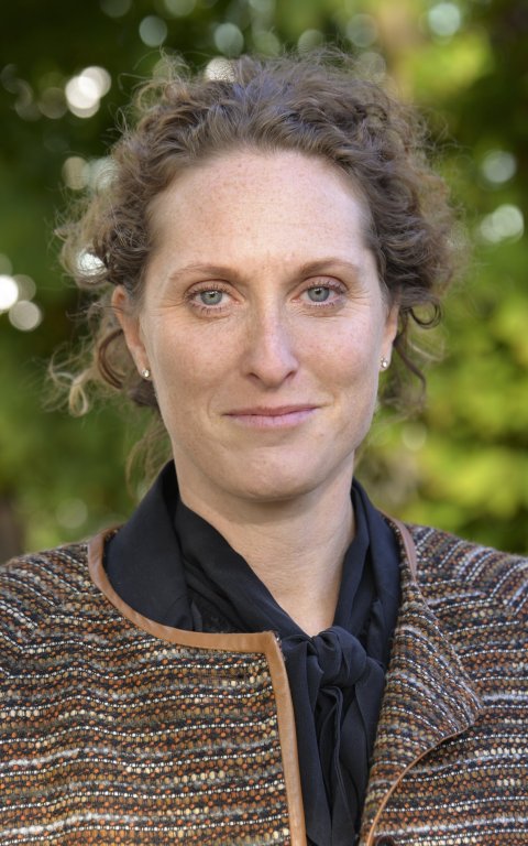 Portrait photo of Caroline Ingre. In the background blurry leaves of a tree can be seen