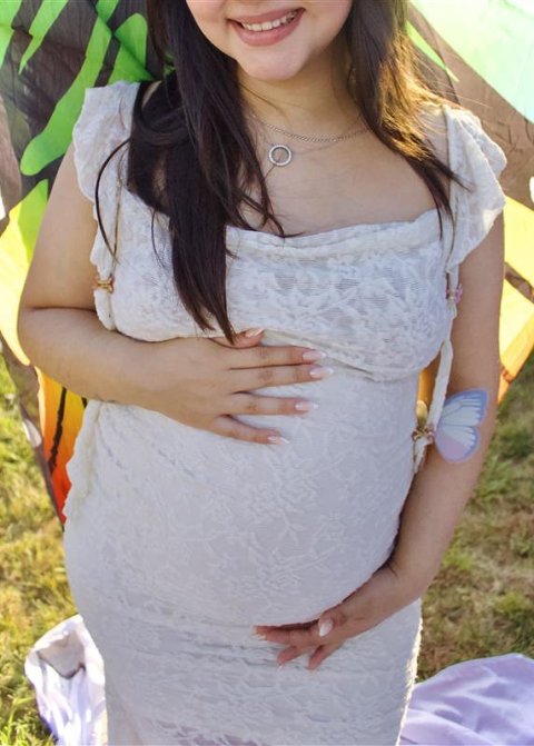 Cropped photo of a smiling pregnant woman holding her swollen baby belly with both hands