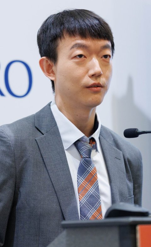 Byoung Hyuck Kim, MD, PhD, standing at a speaker's podium with a microphone in front of him