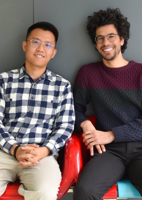 Yimin Zheng und André Rendeiro sitzen nebeneinander auf zwei Schalensitzen aus buntem Kunststoff