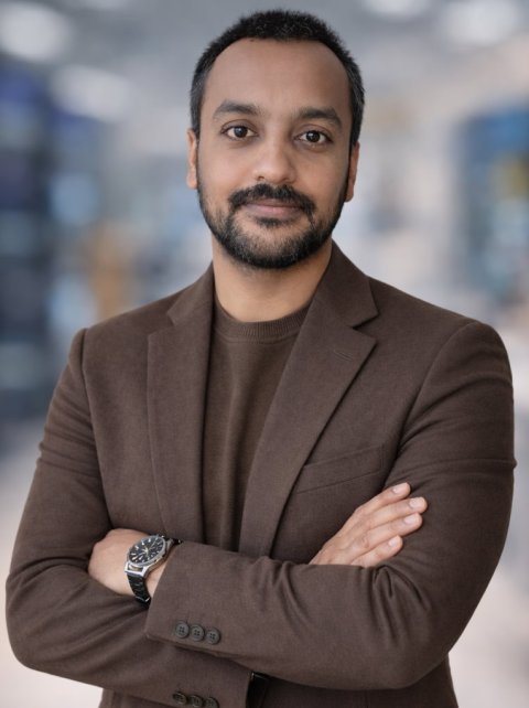Inzamam Mashood Nasir is standing with his arms crossed in front of a blurry background