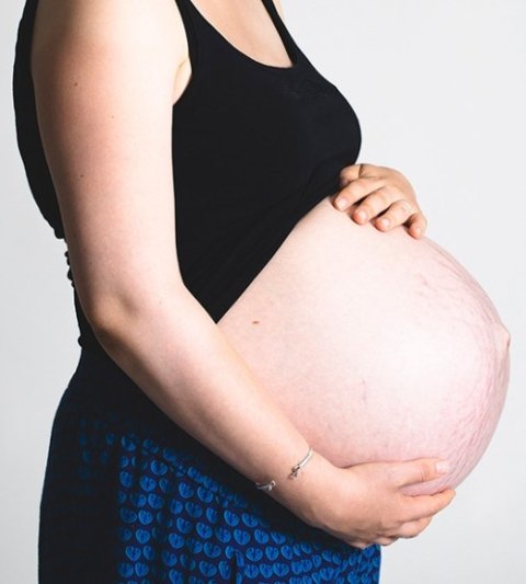 A pregnant woman has one hand under her belly and one on top