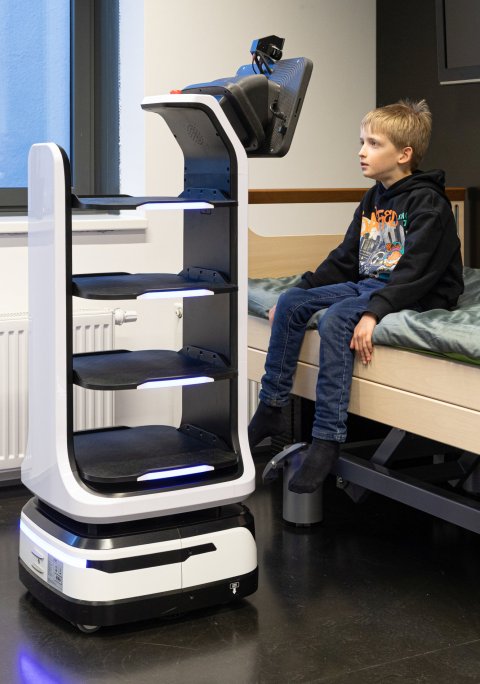 Ein Kind sitzt auf einem Krankenbett, vor ihm ein robotisches Assistenzsystem