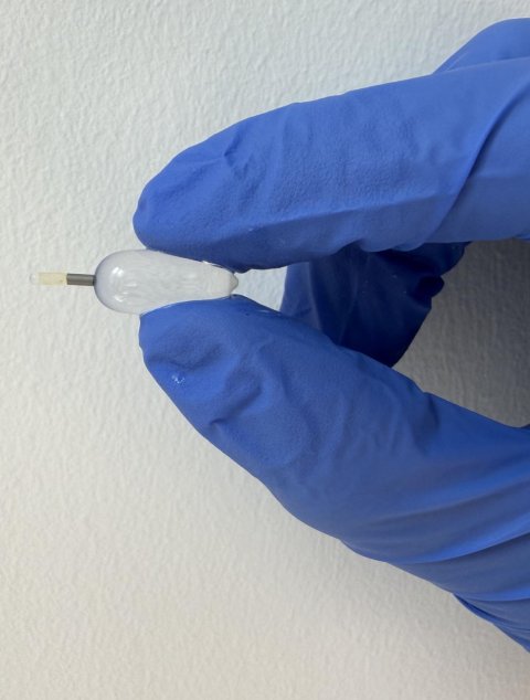 A hand in a protective rubber glove is holding a tiny transparent balloon between its thumb and index finger
