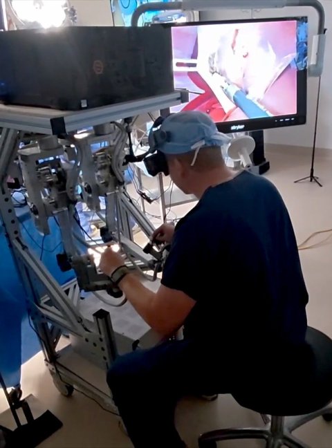 A surgeon sits at a teleoperation console during a surgery