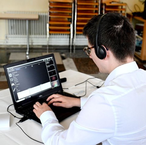 Ein Mann mit Headset bedient einen Laptop auf dem Schreibtisch vor ihm. Auf dem Bildschirm sind medizinische Symbole zu erkennen