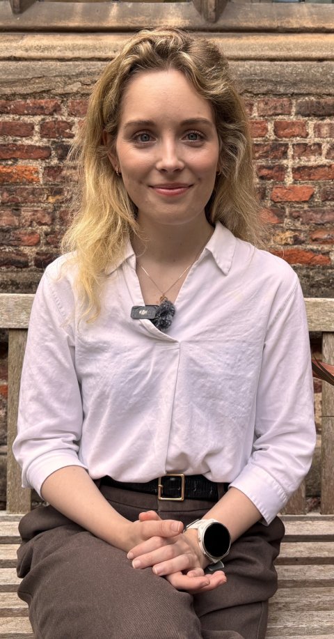 Dr Kim van Daalen is sitting on a wooden bench in front of a red brick house