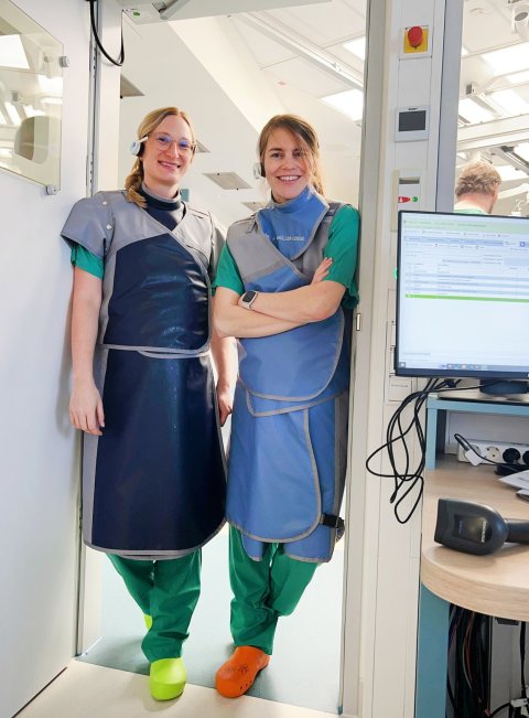 Zwei schwangere Ärztinnen stehen mit Bleischürze zum Schutz vor Strahlung im Herzkatheterlabor eines Krankenhauses
