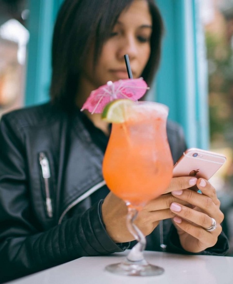 young woman using her smartphone, orange cocktail in the foreground